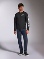 Alpinestars Trackside CSF Tee, Langarmshirt, Schwarz und Weiß, getragen mit dunkelblauer Jeans und schwarzen Sneakern, mit weißem Ride 4.0 Logo auf der Brust und Alpinestars-Schriftzug auf dem Ärmel, lässige vom Motorsport inspirierte Streetwear