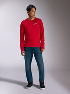 Alpinestars Trackside CSF Tee, Langarmshirt, Rot mit weißem Alpinestars-Logo, Lifestyle-Aufnahme getragen mit blauen Jeans und schwarzen Sneakern, lässige, vom Motorsport inspirierte Sportbekleidung