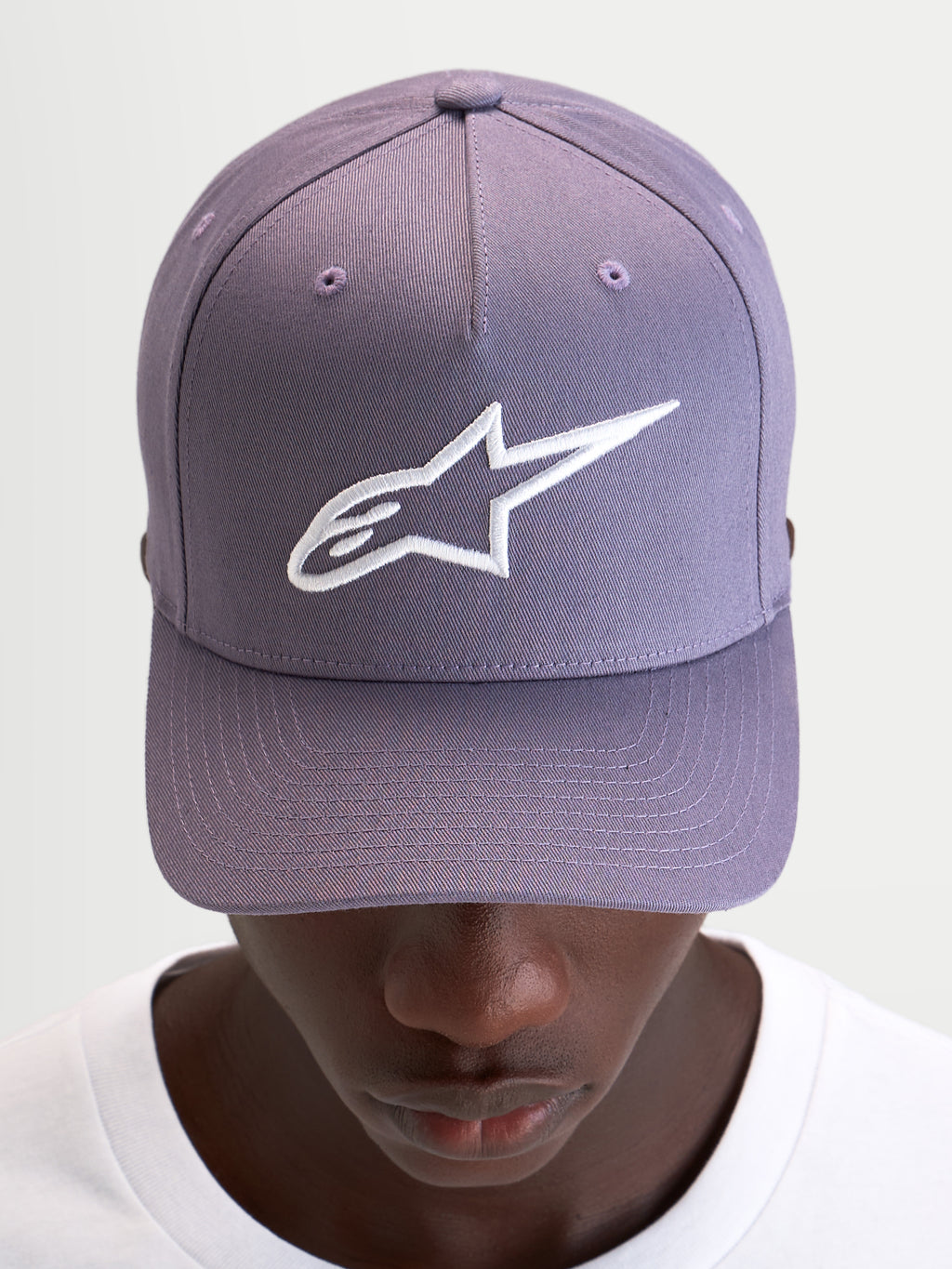 Alpinestars Ageless Snapback Kappe, Freizeitkappe in Staublila und Weiß, mit gebogenem Schirm, strukturierter Krone und aufgesticktem 3D-Astars-Logo auf der Vorderseite, getragen von einem Model