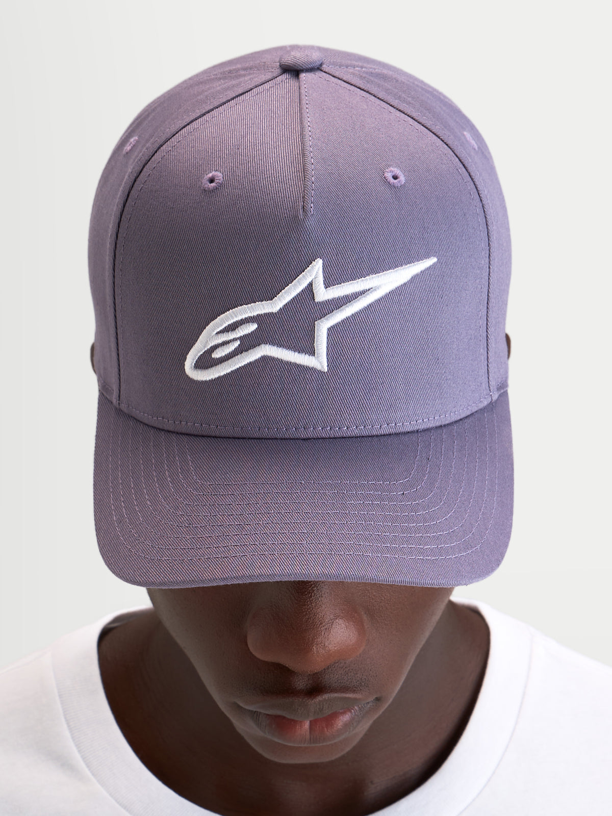 Alpinestars Ageless Snapback Kappe, Freizeitkappe in Staublila und Weiß, mit gebogenem Schirm, strukturierter Krone und aufgesticktem 3D-Astars-Logo auf der Vorderseite, getragen von einem Model