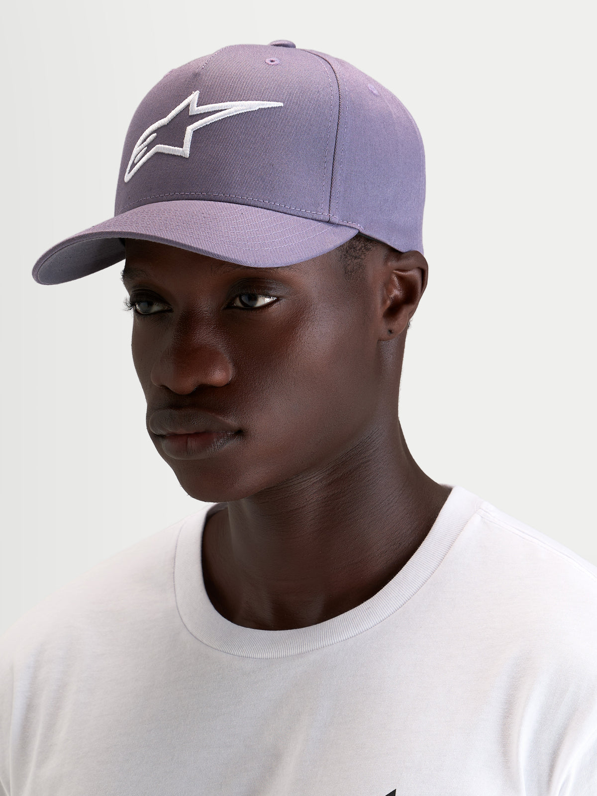 Alpinestars Ageless Snapback Kappe, Sportswear-Cap in Lila und Weiß, getragen von einem Model, mit strukturierter Krone und weißer 3D-Stickerei des Astars-Logos