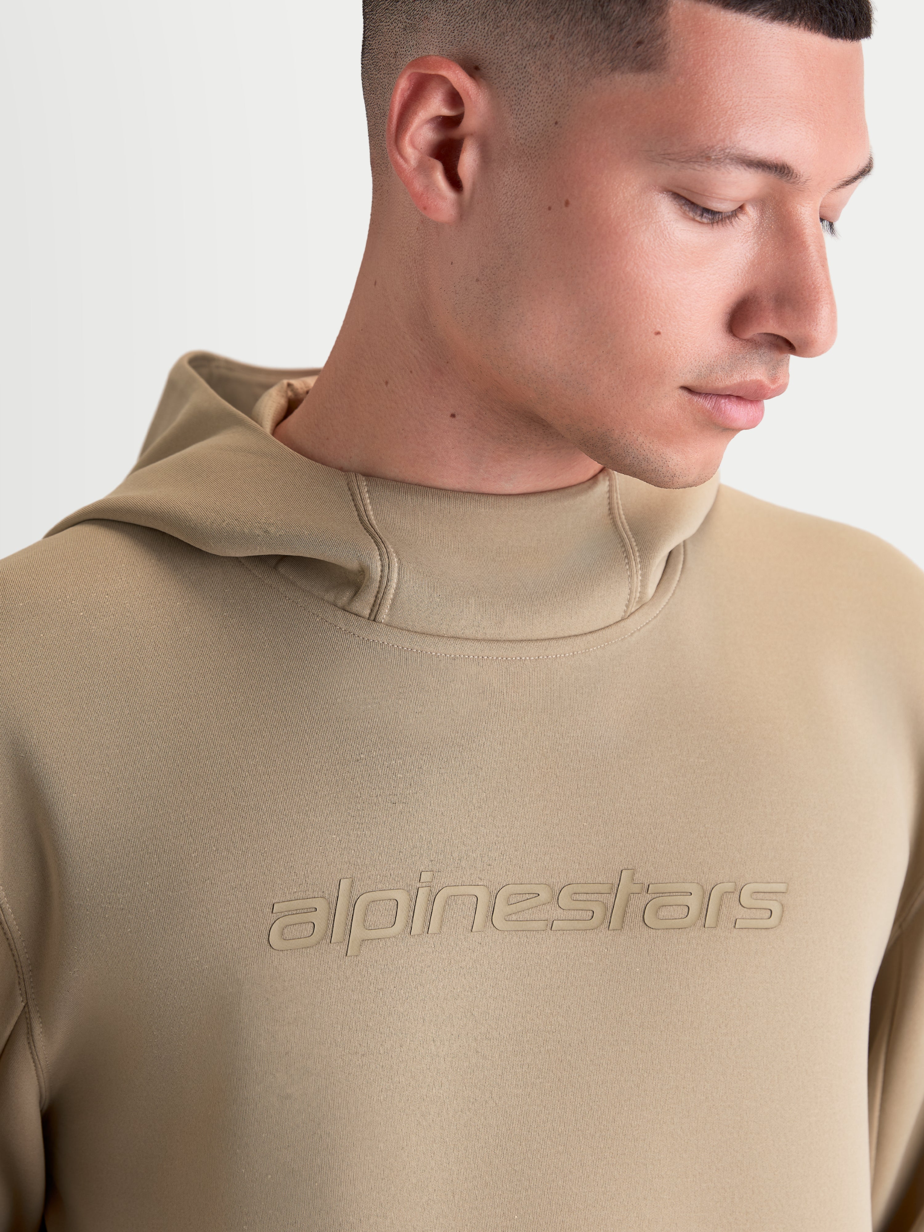 Alpinestars Datrix Hoodie, Sportswear-Pullover für Herren und Damen, Braun, mit tonalem Alpinestars-Logo und mesh-gefütterter Kapuze, Nahaufnahme am Modell zur Darstellung der hochwertigen Fleece-Konstruktion und des Motorsport-Designs.