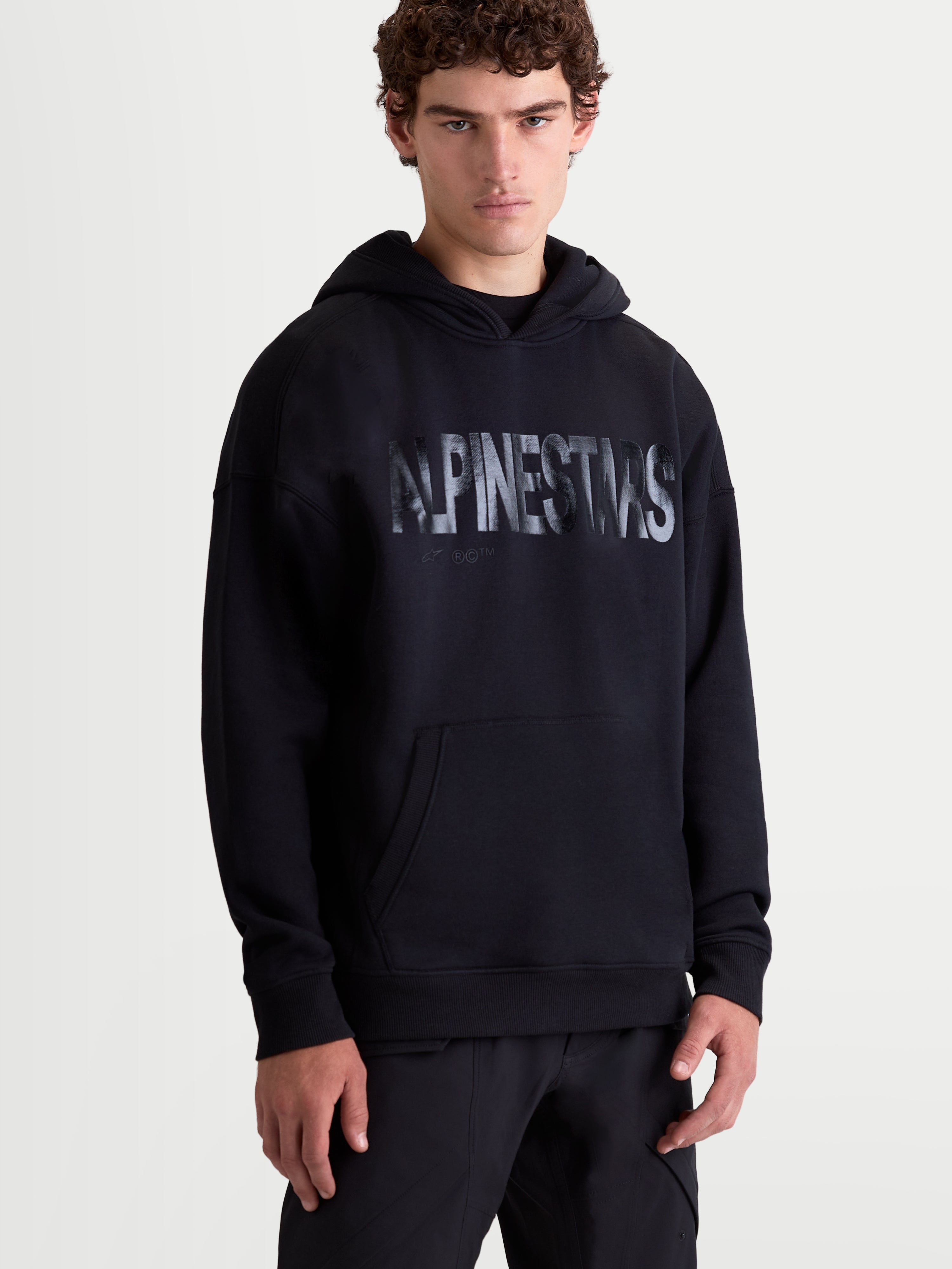 Alpinestars Shaw Oversize-Hoodie, Sportswear-Pullover für den Alltag, Oversize-Passform, Schwarz, mit strukturiertem Wortlogo auf der Brust, Kängurutasche und selbstgefütterter Kapuze, Vorderansicht am Model, weiches Baumwoll-Polyester-Fleece.