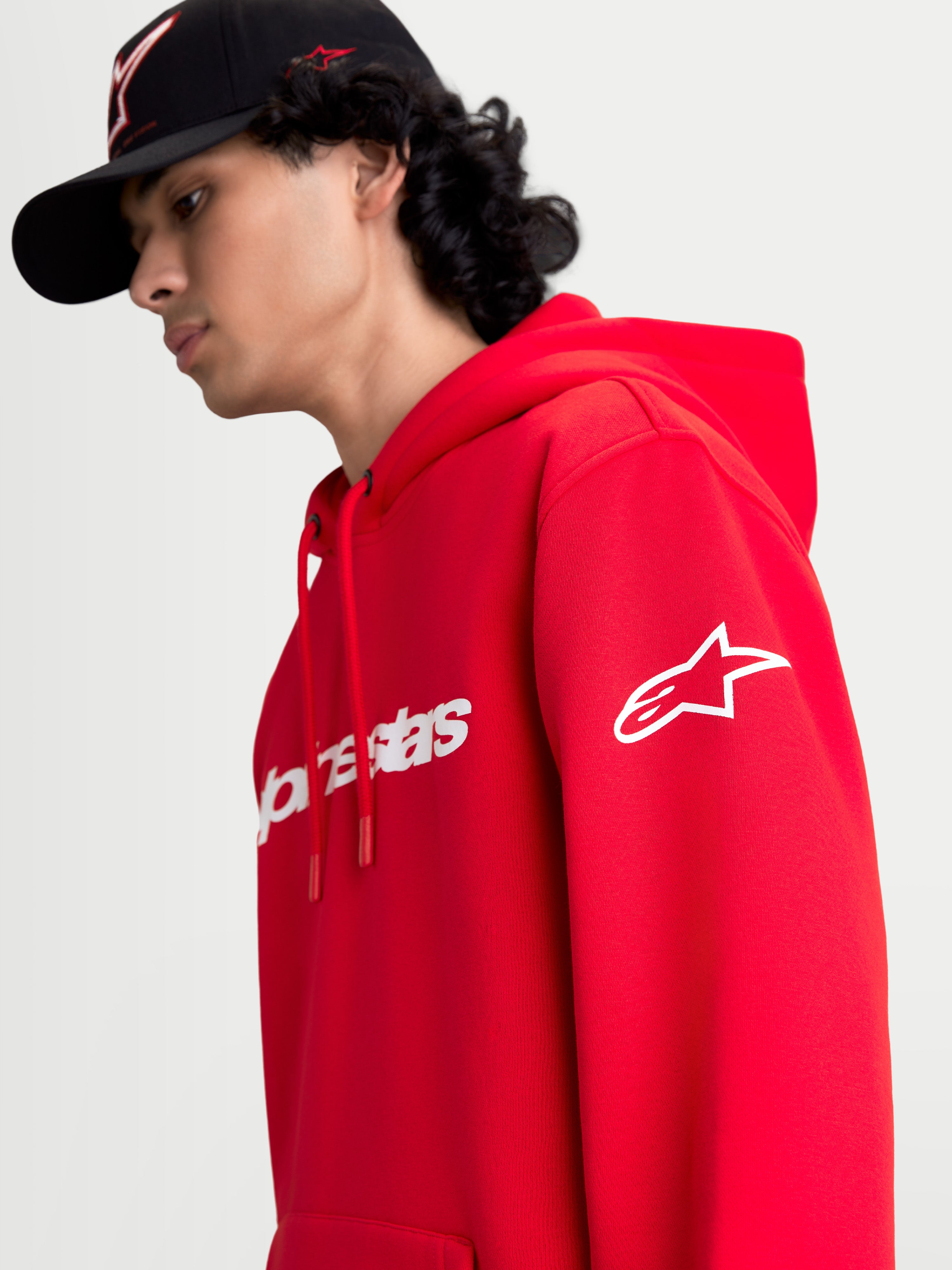 Alpinestars Race Wordmark Hoodie, roter Sportswear-Kapuzenpullover aus Fleece, Ansicht am Modell mit weißem Alpinestars Ageless-Logo am Ärmel und Race Linear Branding auf der Vorderseite, lässiges Motorsport-Design.