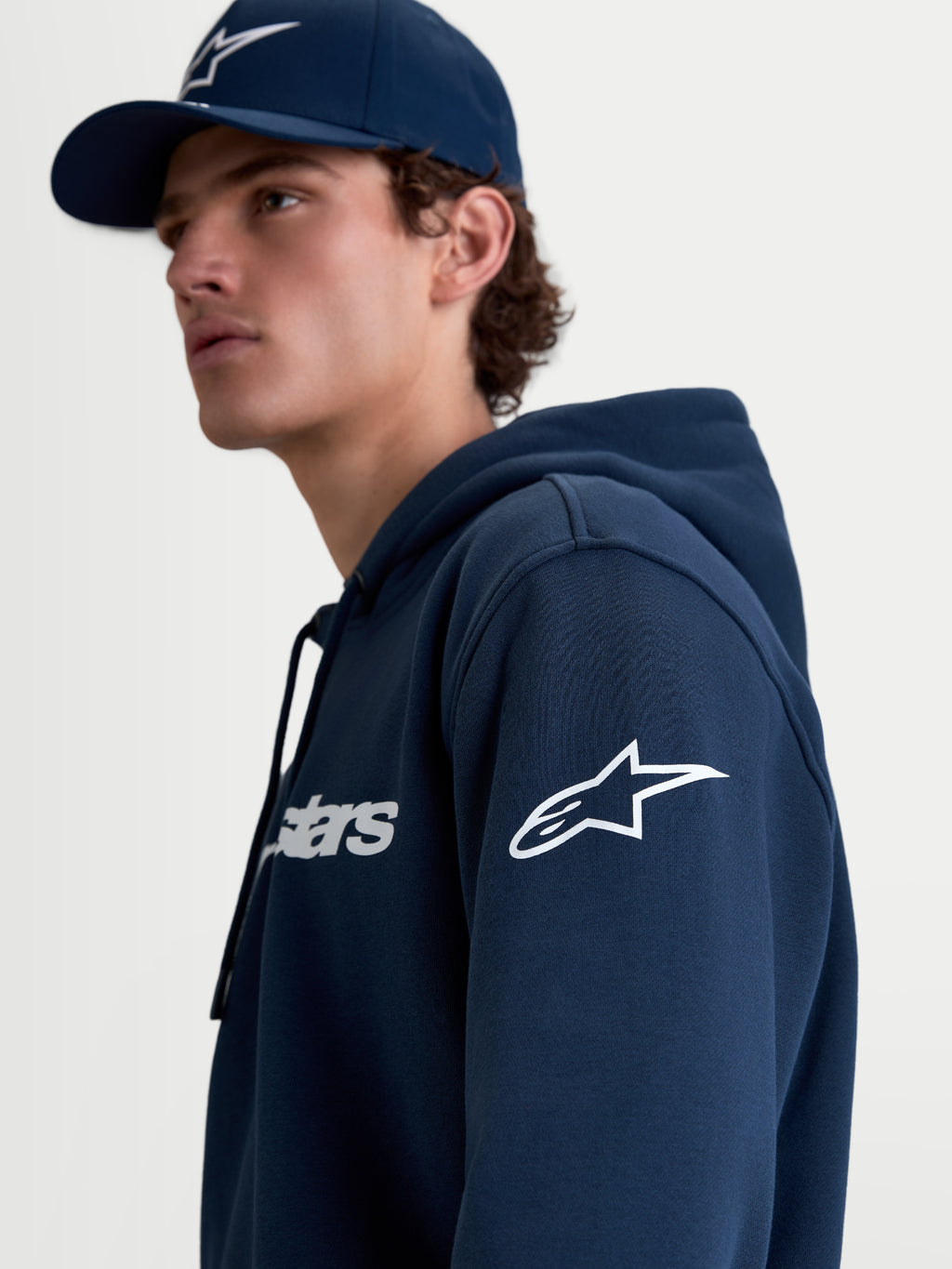 Alpinestars Race Wordmark Hoodie, Herren-Sportswear-Kapuzenpullover aus Fleece in Blau und Weiß, mit weißem Ageless-Logo am Ärmel und Race-Schriftzug auf der Brust, Lifestyle-Ansicht am Model.