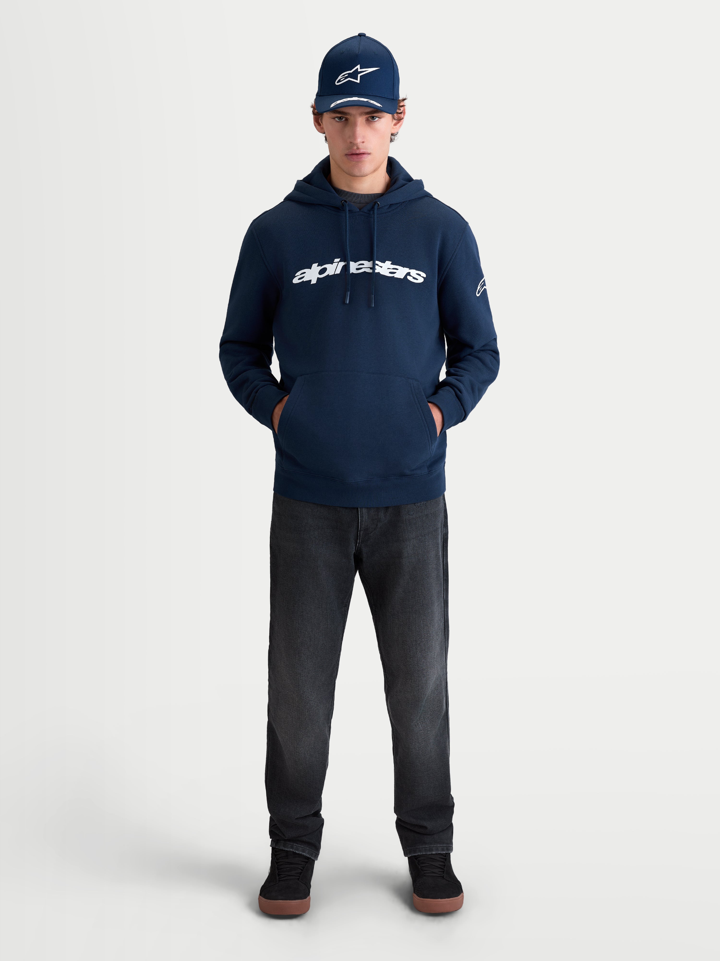 Alpinestars Race Wordmark Hoodie, Sportswear-Kapuzenpullover aus Fleece, Blau und Weiß, mit markanter Logo-Grafik auf der Brust und Ageless-Ärmellogo, Lifestyle-Ansicht am Modell für einen lässigen Motorsport-Look.