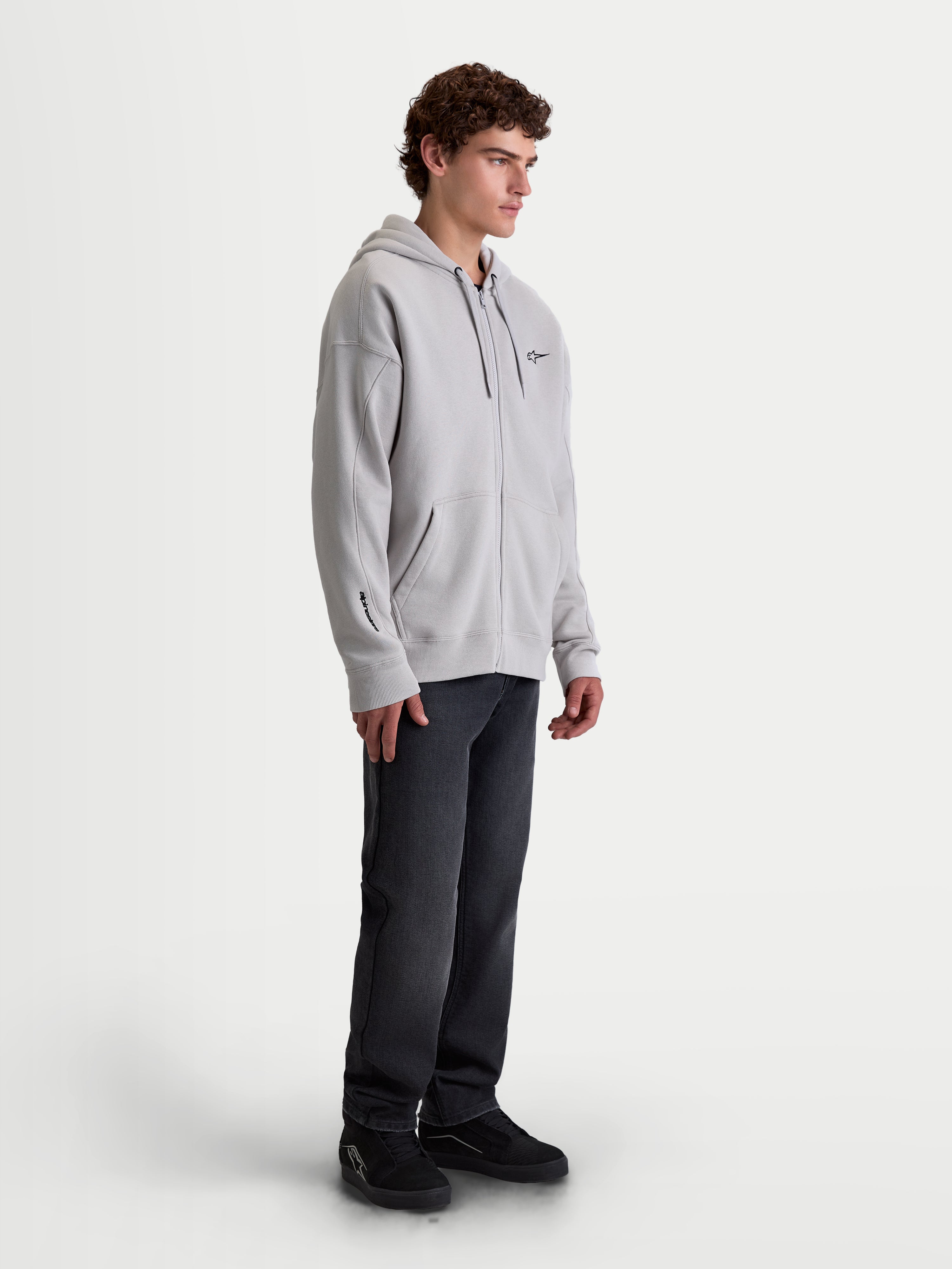 Alpinestars Entity Oversized Hoodie, Herren-Sportswear-Zip-Fleecejacke, Zementgrau, mit entspannter Passform, Vislon-Frontreißverschluss, selbstgefütterter Kapuze und Kängurutasche. On-Model-Aufnahme mit Stickerei-Details an Brust und Ärmel, entworfen für den lässigen Lifestyle und Motorsport-Enthusiasten.
