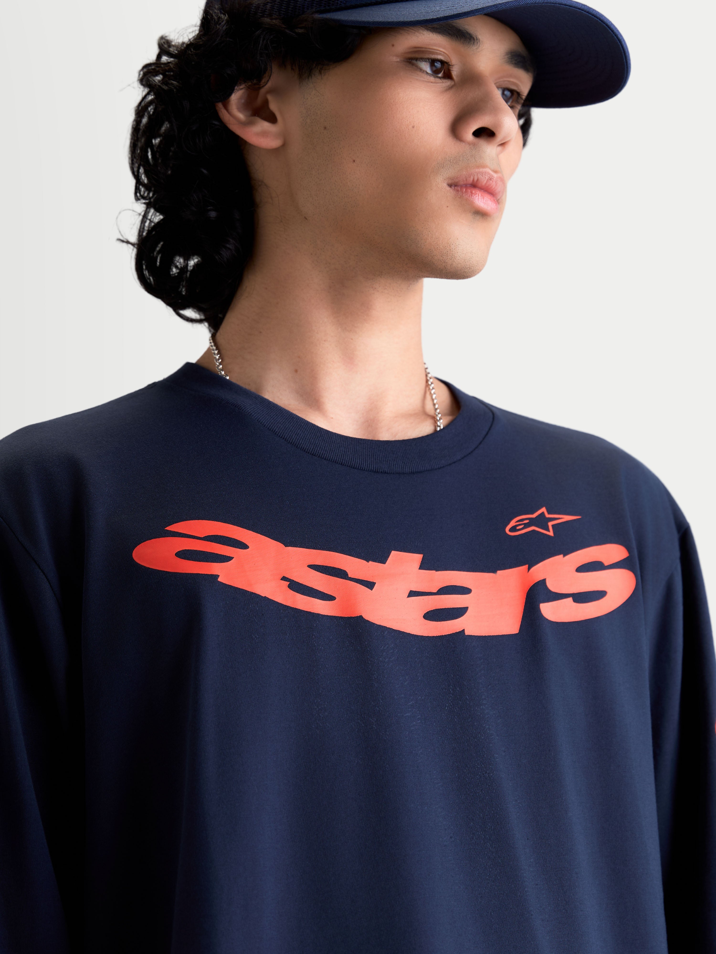 Alpinestars Velocifier CSF Langarm-T-Shirt, Motorsport-inspirierte Freizeit-Sportswear am Model, Dunkelblau mit gebogener orangefarbener Astars-Brustgrafik, weiche Baumwollmischung.