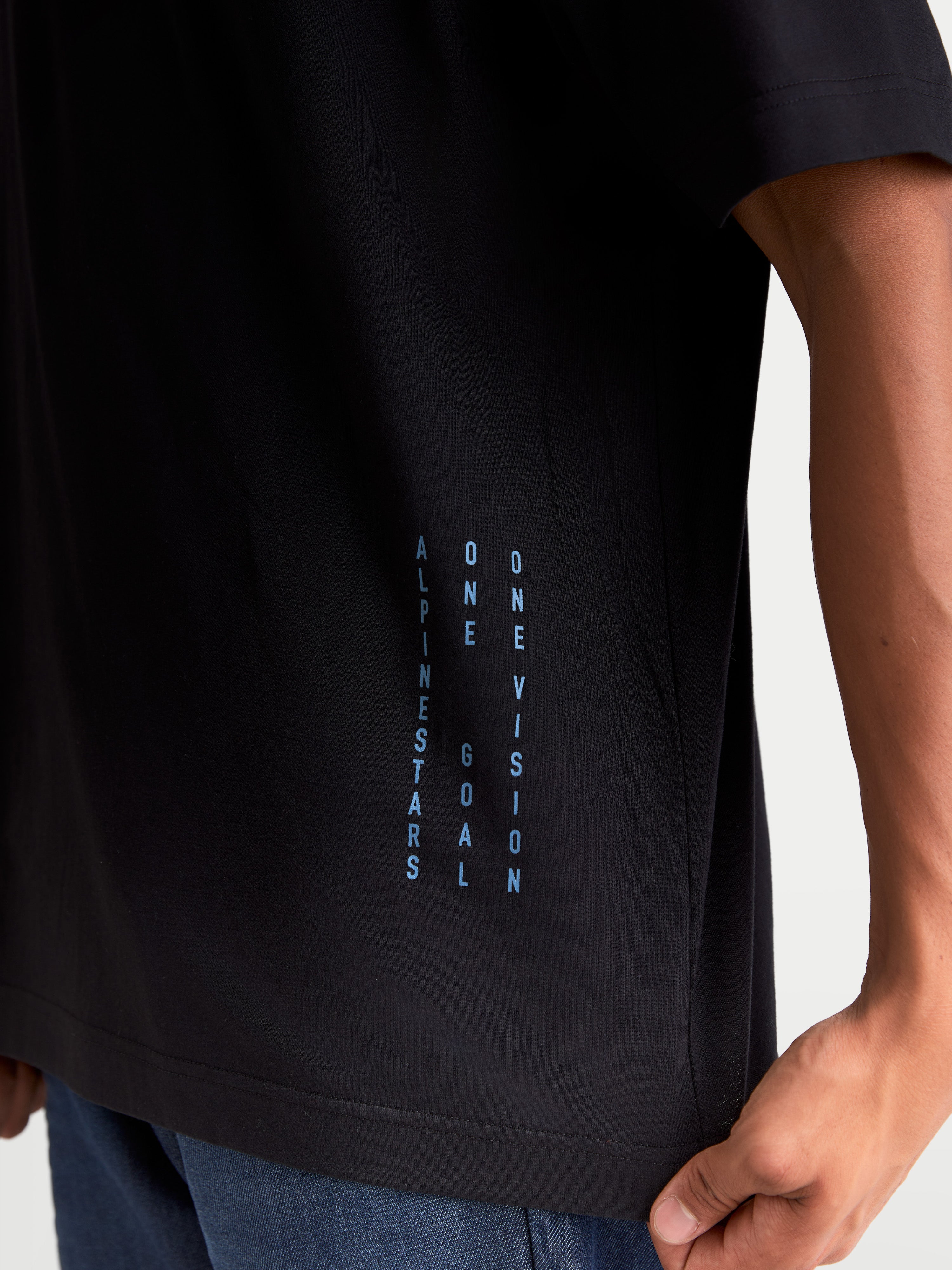 Alpinestars Chalk Oversized CSF T-Shirt, Kurzarm-Sportswear-T-Shirt, Schwarz und Blau, mit vertikalem ONE GOAL ONE VISION Branding an der Seite, entspannte Oversized-Passform, Detailansicht am Model.