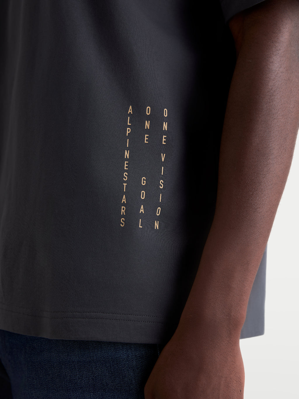 Alpinestars Chalk Oversized CSF T-Shirt, Unisex Sportswear T-Shirt in Grau, Detailaufnahme des vertikalen Brandings mit dem 'ONE GOAL ONE VISION' Manifest, hochwertiges Baumwoll-Polyester-Mischgewebe, Motorsport-inspirierte Freizeitkleidung.
