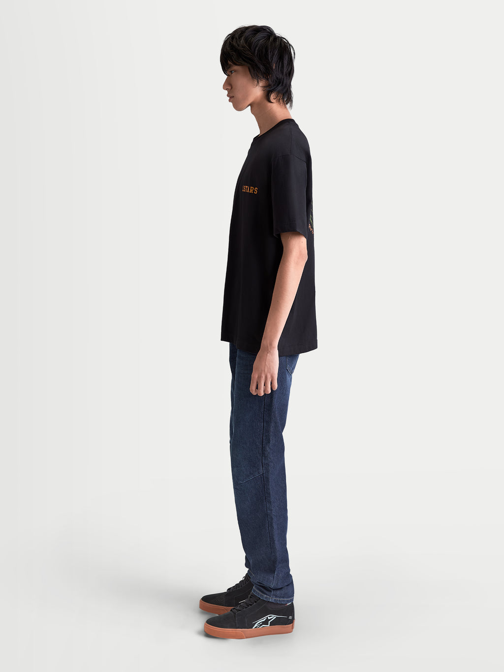 Alpinestars Latitude Oversized CSF T-Shirt, Kurzarm-Sportswear-T-Shirt für Herren, Schwarz mit orangefarbener Astars-Grafik, Seitenansicht am Modell, lässige Oversized-Passform, hochwertiger Lifestyle-Look.