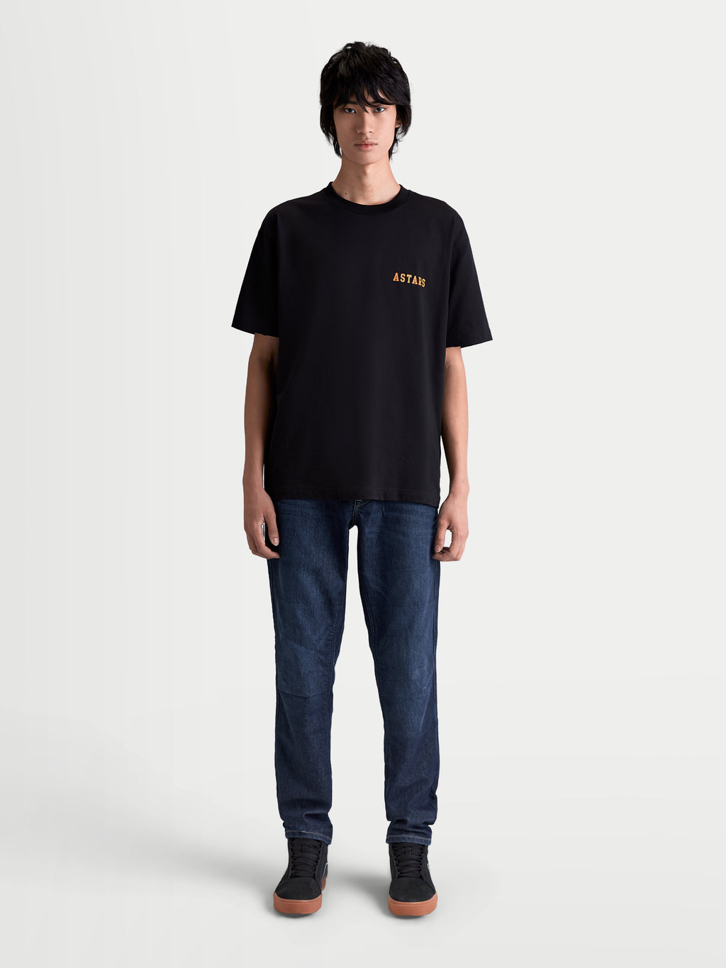 Alpinestars Latitude Oversized CSF T-Shirt, Kurzarm-Sportswear-T-Shirt, Schwarz und Orange, lässige Oversized-Passform, hochwertige Baumwoll-Polyester-Mischung, mit ASTARS Brustgrafik am Model präsentiert.