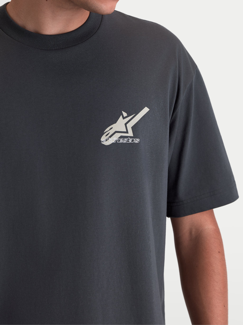 Alpinestars Ghost Oversized CSF T-Shirt, Kurzarm-Sportswear-T-Shirt, Anthrazit, Nahaufnahme der Astars-Logo-Grafik auf der Brust, Baumwoll-Polyester-Mischung mit lockerer Passform, Lifestyle-Detail am Model.