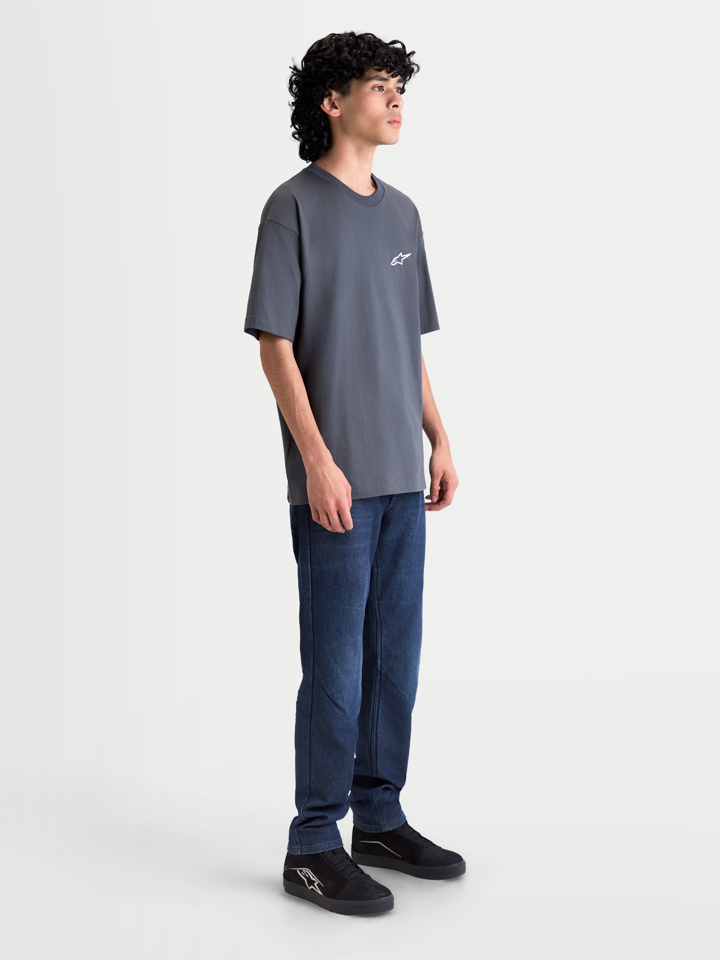 Alpinestars Mandate Oversized CSF T-Shirt, Unisex Kurzarm-Sportswear-T-Shirt, Grau-Anthrazit, mit lockerer Oversized-Passform und Astars-Logo im Puff-Druck, Seitenansicht am Model.