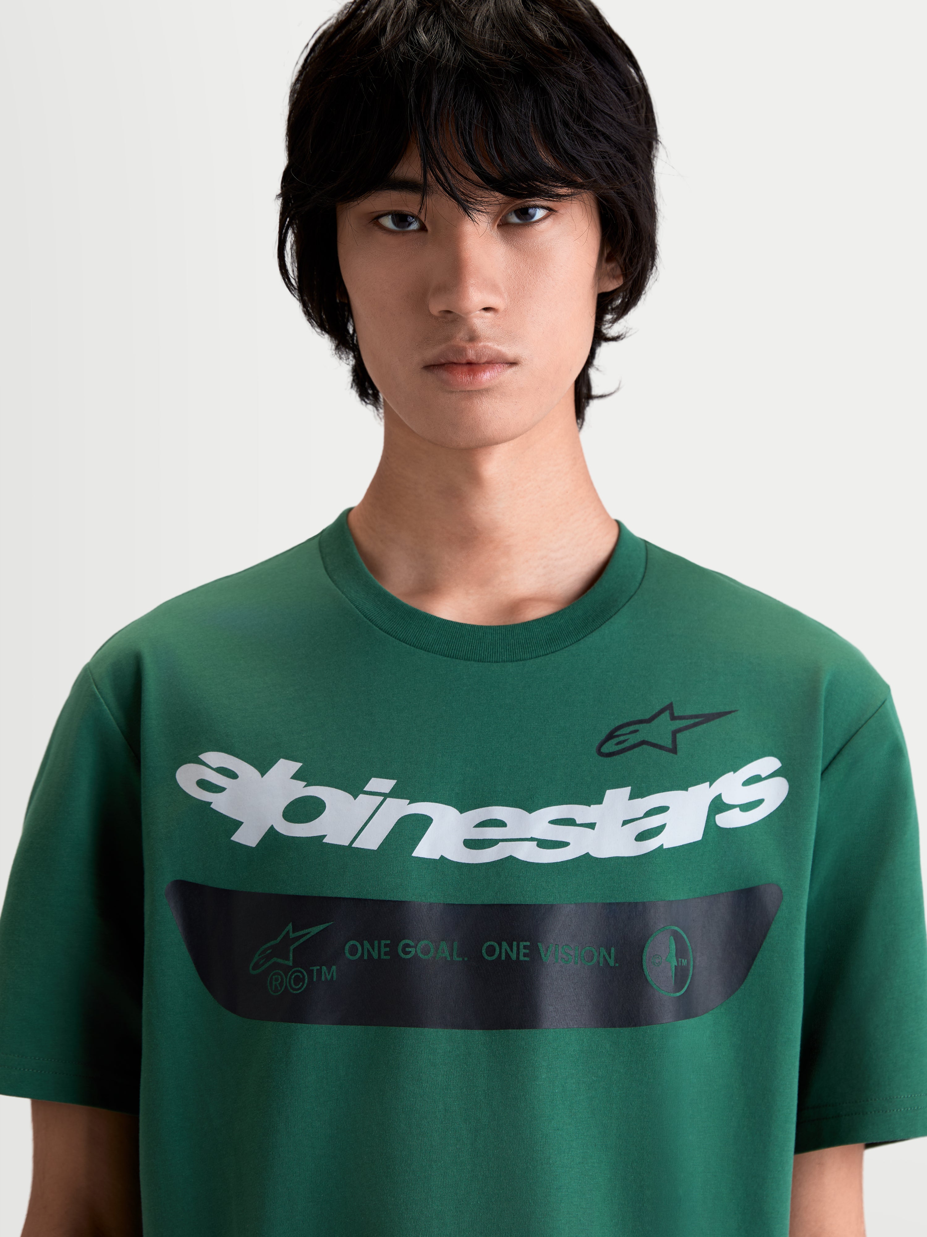 Alpinestars Singular CSF T-Shirt, Herren-Kurzarm-T-Shirt in Grün, Sportswear mit weißer gebogener Alpinestars Wortgrafik und schwarzem Band mit dem One Goal One Vision Motto, Premium-Baumwoll-Polyester-Mischung für Alltagskomfort, am Model.