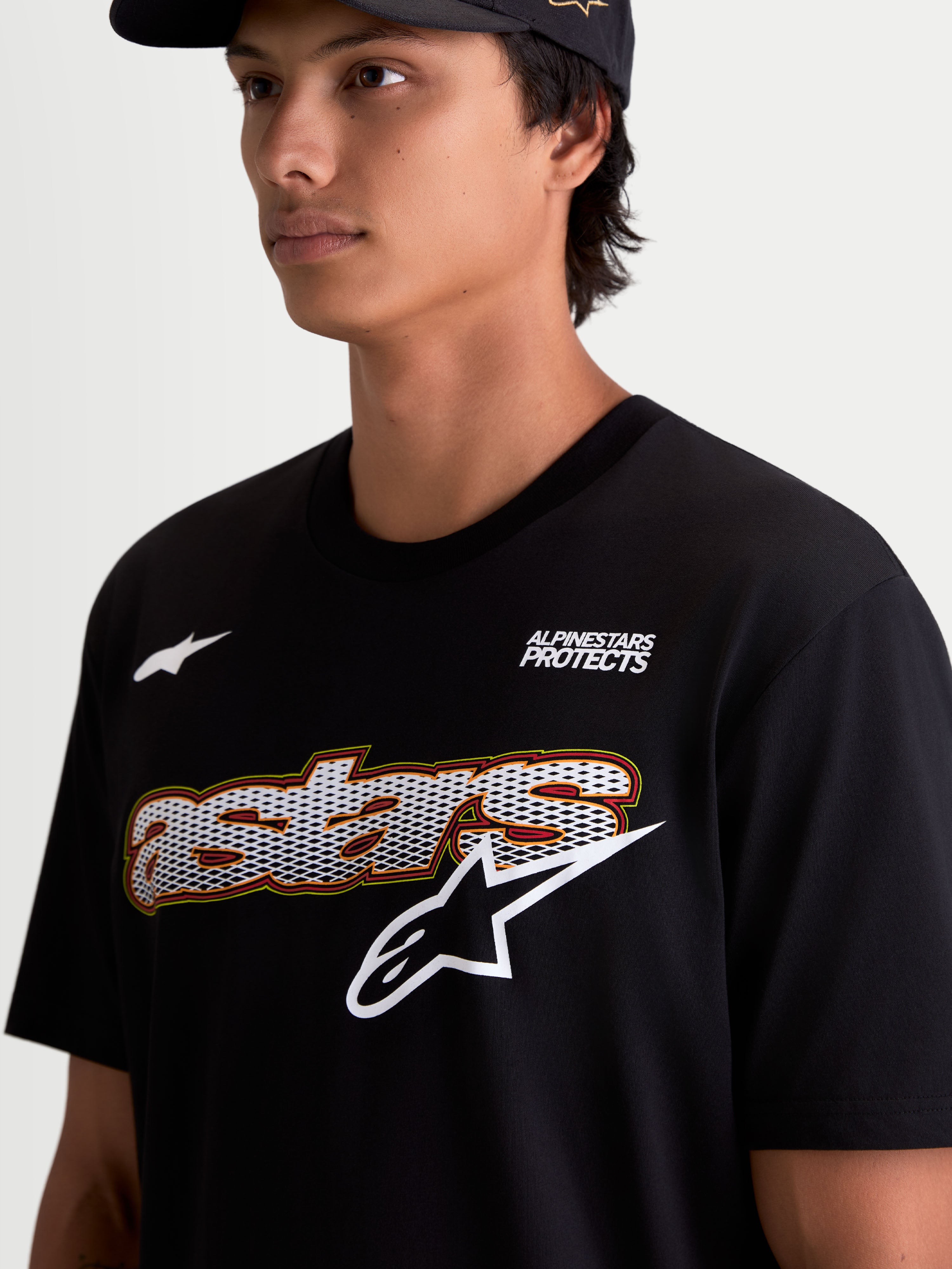 Alpinestars Cypress CSF T-Shirt, Kurzarm-Sportswear-T-Shirt für Herren, Schwarz, Nahaufnahme am Model mit Brustgrafik inklusive Astars-Wortmarke mit Mesh-Füllung, „Alpinestars Protects“-Branding und weißem Logo, Baumwoll-Polyester-Mischgewebe.