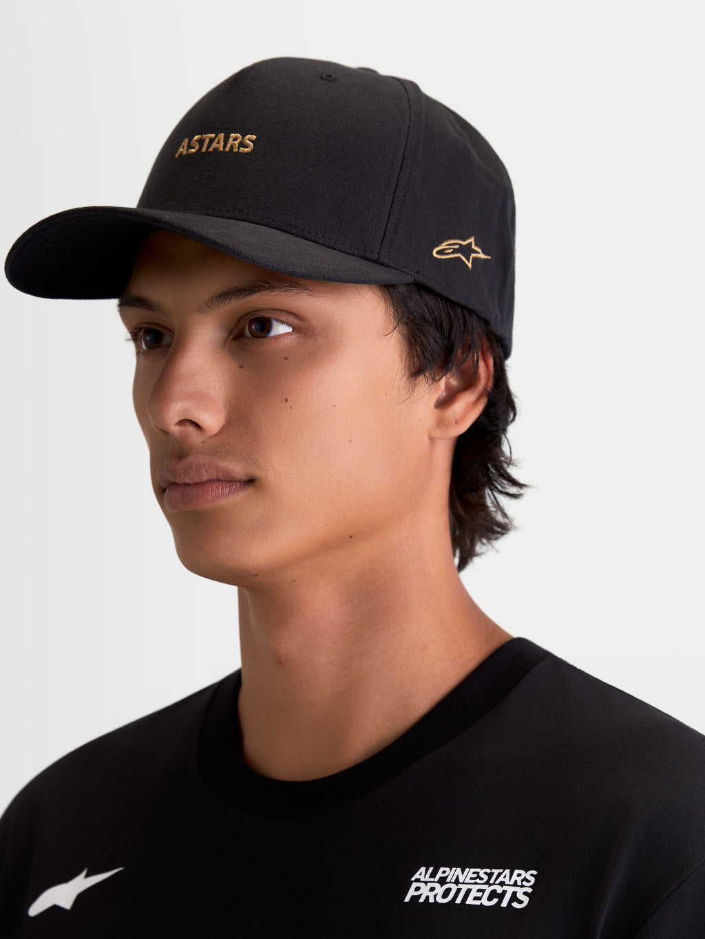 Alpinestars County Canvas Kappe, schwarze Sportswear-Kappe mit goldener ASTARS-Logostickerei auf der Vorderseite und seitlich, gebogener Schirm und strukturierte Krone, Oxford-Peach-Gewebe, motorsport-inspirierter Lifestyle-Look am Modell.