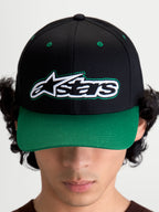 Alpinestars Retro Snapback Kappe, Motorsport-inspirierte Sportswear-Baseballkappe mit gebogenem Schirm und strukturierter Krone, Unisex, Schwarz und Grün, Baumwolltwill, Frontansicht am Modell mit Astars-Logo und grünem Kontrast-Zierstich.