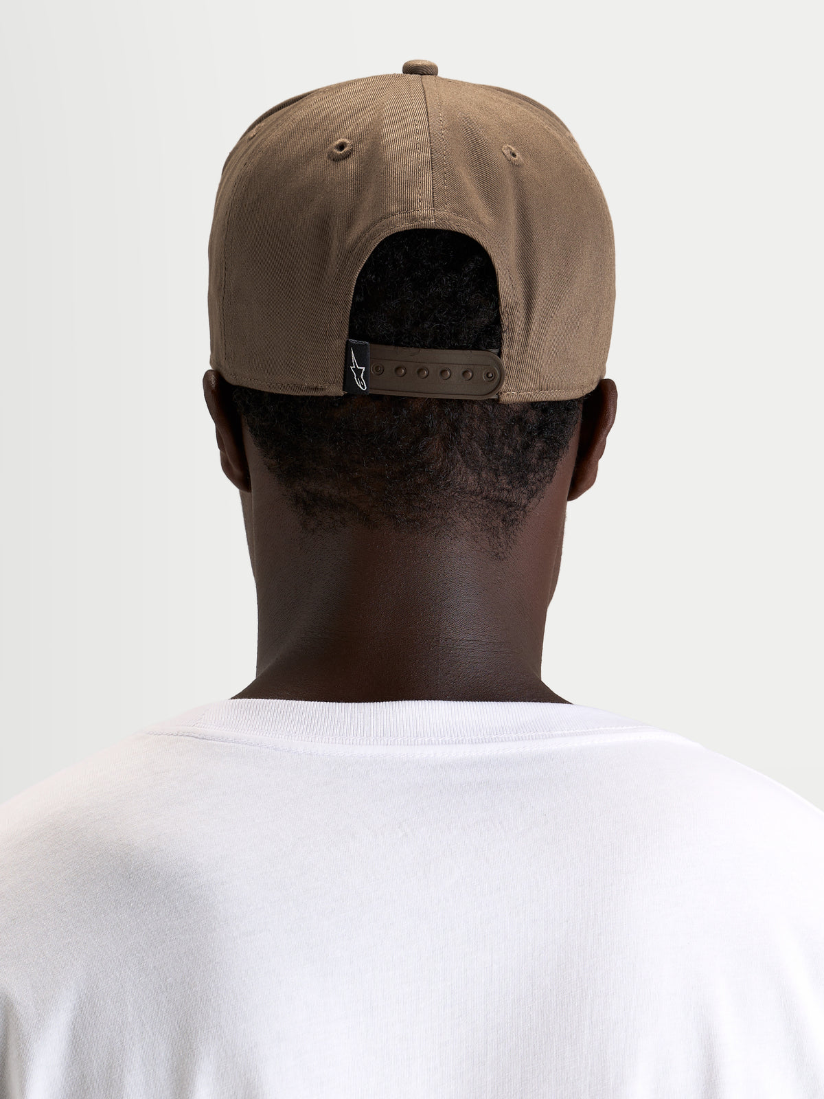Alpinestars Acme Snapback Kappe, braune Sportswear-Kappe rückwärts getragen von einem Model, mit verstellbarem Snapback-Verschluss und Markenlabel hinten