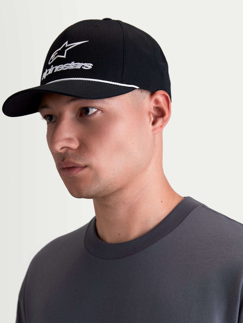 Alpinestars Combo Logo Snapback-Kappe, Sportswear-Lifestyle-Kappe in Schwarz und Weiß, mit gebogenem Schirm, strukturierter Krone, weißer Alpinestars Combo-Logo-Stickerei und Kordel-Detail, am Modell in der Profilansicht gezeigt.