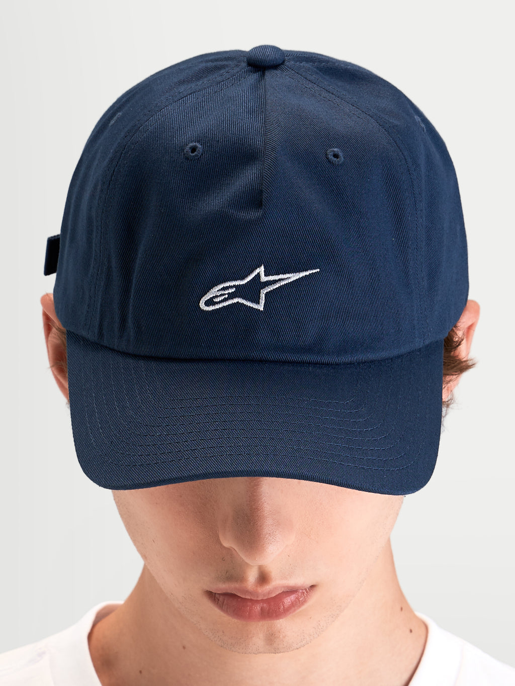 Alpinestars Dylan Dad-Kappe, blaue Baumwolltwill-Sportswear-Kappe mit gebogenem Schirm und weißer Astars-Logo-Stickerei auf der Vorderseite, getragen von einem Model