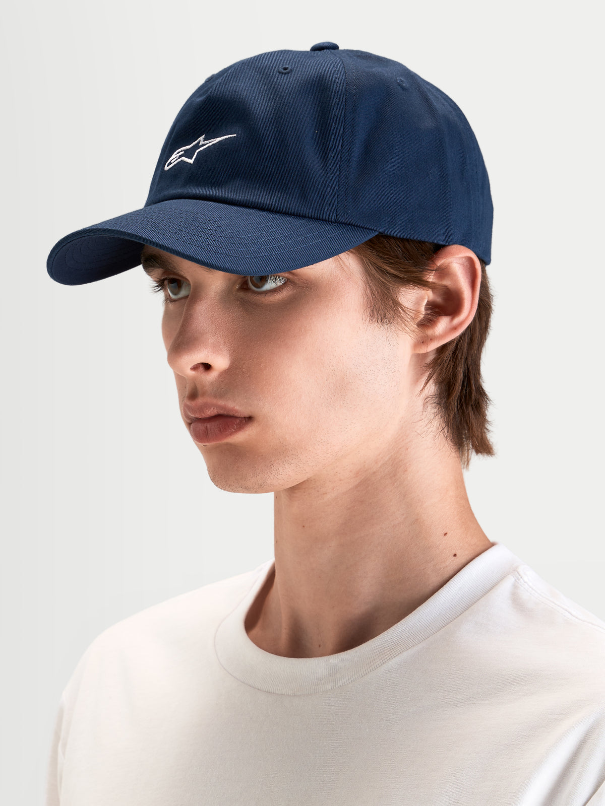 Alpinestars Dylan Dad-Kappe, lässige Sportswear-Kappe in Marineblau, getragen von einem Model, mit gebogenem Schirm, unstrukturierter niedriger Krone und weißer Astars-Logo-Stickerei auf der Vorderseite