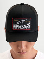 Alpinestars Hemmings Trucker-Kappe, Sportswear-Snapback-Cap in Schwarz, getragen von einem Model, mit gewebtem Alpinestars Logo-Patch auf der Vorderseite und atmungsaktiven Mesh-Rückeneinsätzen