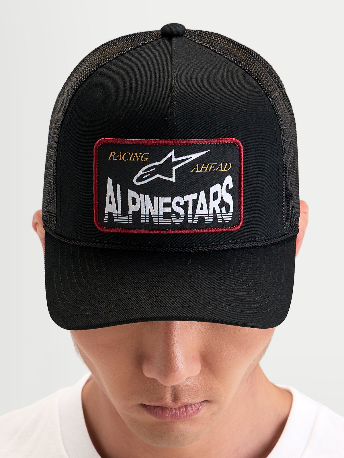Alpinestars Hemmings Trucker-Kappe, Sportswear-Snapback-Cap in Schwarz, getragen von einem Model, mit gewebtem Alpinestars Logo-Patch auf der Vorderseite und atmungsaktiven Mesh-Rückeneinsätzen