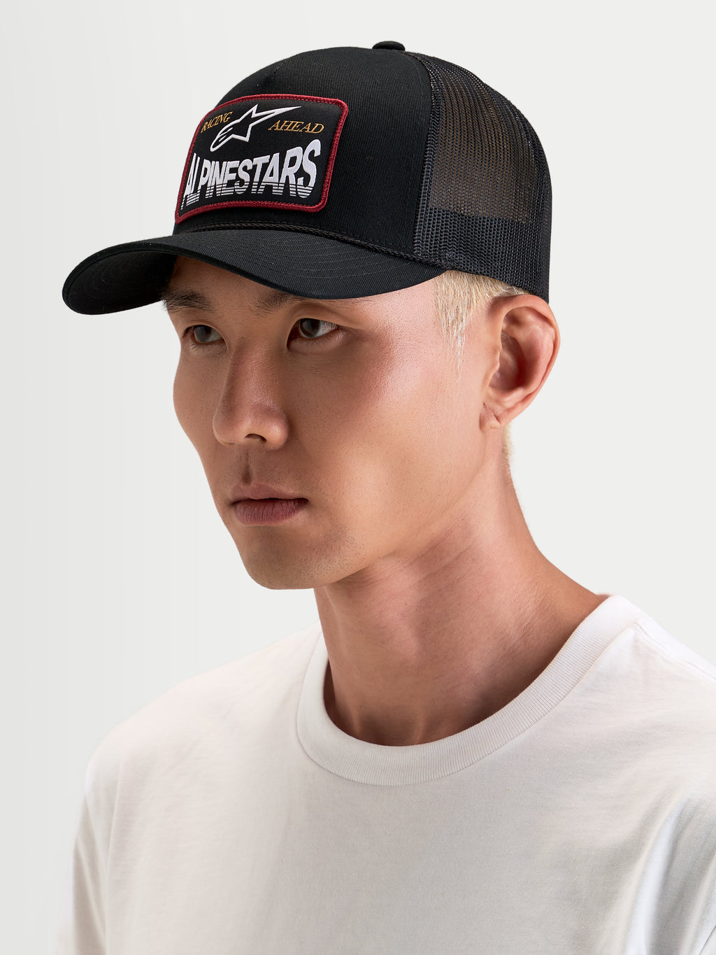Alpinestars Hemmings Trucker-Kappe, schwarze Sportswear-Snapback-Kappe getragen von einem Model, mit atmungsaktiven Mesh-Rückeneinsätzen und gewebtem Alpinestars Logo-Patch auf der Vorderseite
