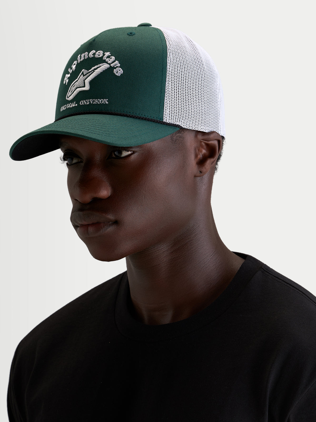 Alpinestars Baron Trucker-Kappe, grüne und weiße Trucker-Mütze für Sportswear, getragen von einem männlichen Model, mit gebogenem Schirm, strukturierter Twill-Front, atmungsaktiver Mesh-Rückseite und gesticktem Logo vorne