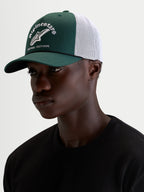 Alpinestars Baron Trucker-Kappe, grüne und weiße Trucker-Mütze für Sportswear, getragen von einem männlichen Model, mit gebogenem Schirm, strukturierter Twill-Front, atmungsaktiver Mesh-Rückseite und gesticktem Logo vorne