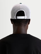 Alpinestars Baron Trucker-Kappe, lässige Sportswear-Mesh-Cap, getragen von einem Model, Rückansicht mit verstellbarem Snapback-Verschluss, weißen Poly-Mesh-Einsätzen und grünem Kronenknopf