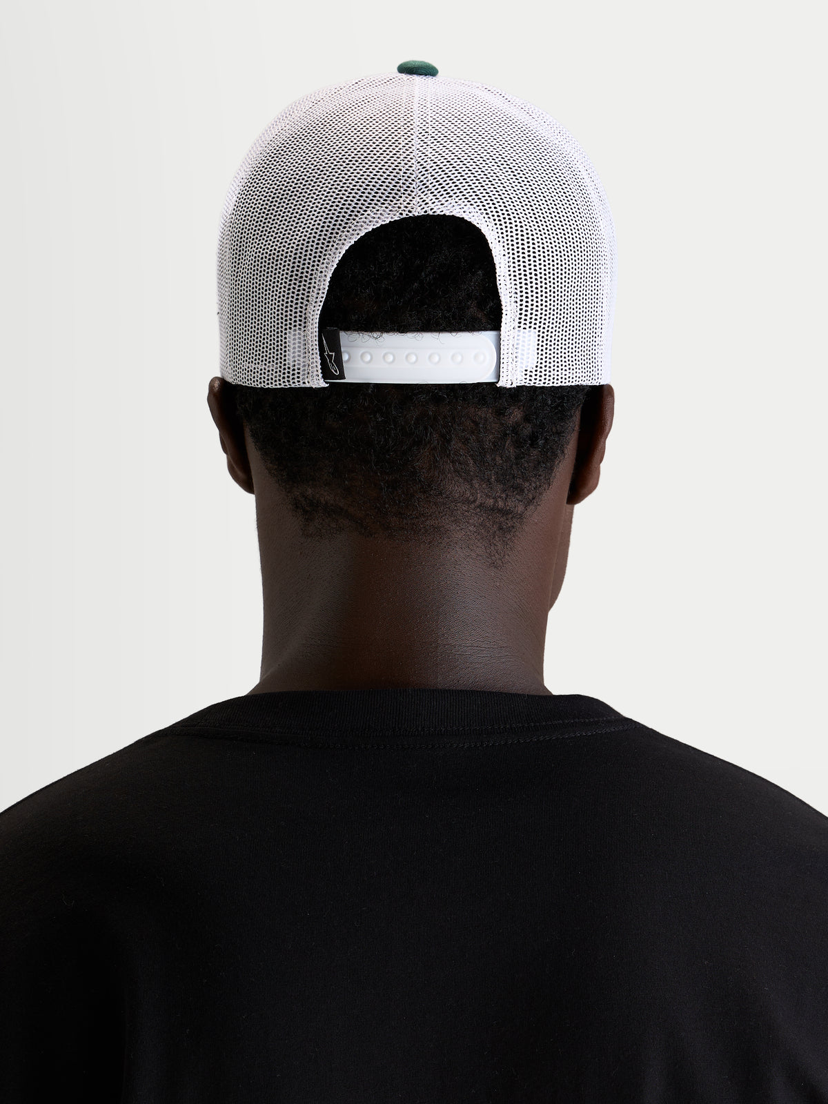 Alpinestars Baron Trucker-Kappe, lässige Sportswear-Mesh-Cap, getragen von einem Model, Rückansicht mit verstellbarem Snapback-Verschluss, weißen Poly-Mesh-Einsätzen und grünem Kronenknopf