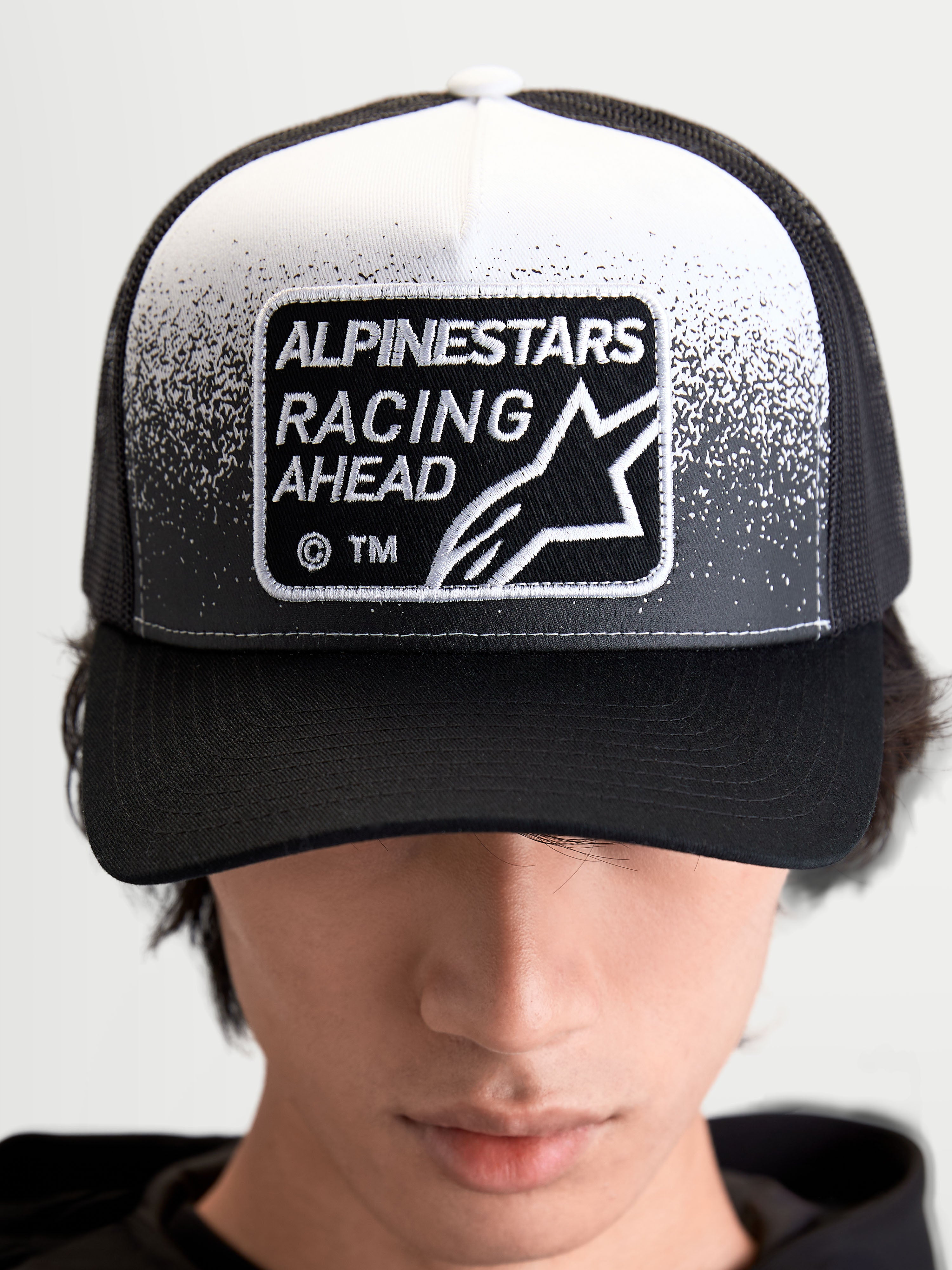 Alpinestars Gravel Trucker-Kappe, Sportswear Trucker-Cap für Damen und Herren, Schwarz und Weiß, mit gewebtem Alpinestars Racing Ahead Patch, Kieselstruktur-Details, strukturierter Krone und gebogenem Schirm, Frontansicht am Modell.