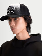 Alpinestars Gravel Trucker-Kappe, Sportswear-Mütze auf Model, Schwarz und Weiß, mit strukturierter Krone, gebogenem Schirm, atmungsaktiver Mesh-Rückseite und gewebtem Patch mit Kieselstruktur-Grafik und Alpinestars Racing Ahead Branding.