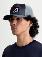 Alpinestars Gravel Trucker-Kappe am Modell, Sportswear-Kappe in Dunkelgrau und Schwarz mit hellgrauem Mesh-Rücken, strukturierte Krone, gebogener Schirm und gewebter Front-Patch mit rotem Alpinestars-Schriftzug, ideal für einen Motorsport-inspirierten Lifestyle.