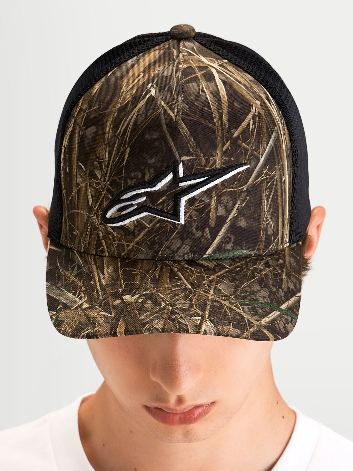Alpinestars Thicket Realtree Trucker-Kappe, Sportswear Trucker-Mütze in Realtree-Camo und Schwarz, getragen von einem Model, mit gebogenem Schirm, strukturierter Krone und weißem, gesticktem Astars-Logo auf der Front