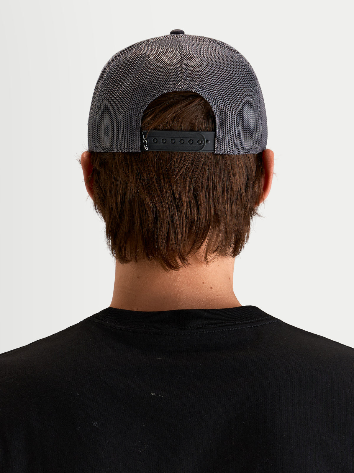 Alpinestars Ten Trucker Hat, sportswear snapback cap in dark grey, rear view on a model showing the adjustable snapback closure, mesh back panels, and back labeling detail
