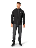 Alpinestars Kascade Regenjacke, Herren-Regenjacke, Schwarz, kombiniert mit dunkelgrauen Jeans und schwarzen Sneakern, mit Kapuzendesign, beschichtetem Frontreißverschluss und weißem Alpinestars-Logo auf der Brust, lässige, vom Motorsport inspirierte Streetwear