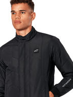 Alpinestars Precedent Jacke, gesteppte Sportswear-Jacke für Herren in Schwarz, Nahaufnahme mit niedrigem Stehkragen, Logo-Patch auf der Brust und Ärmelstickerei, ikonisches schräges Steppmuster für einen vom Motorsport inspirierten Look.