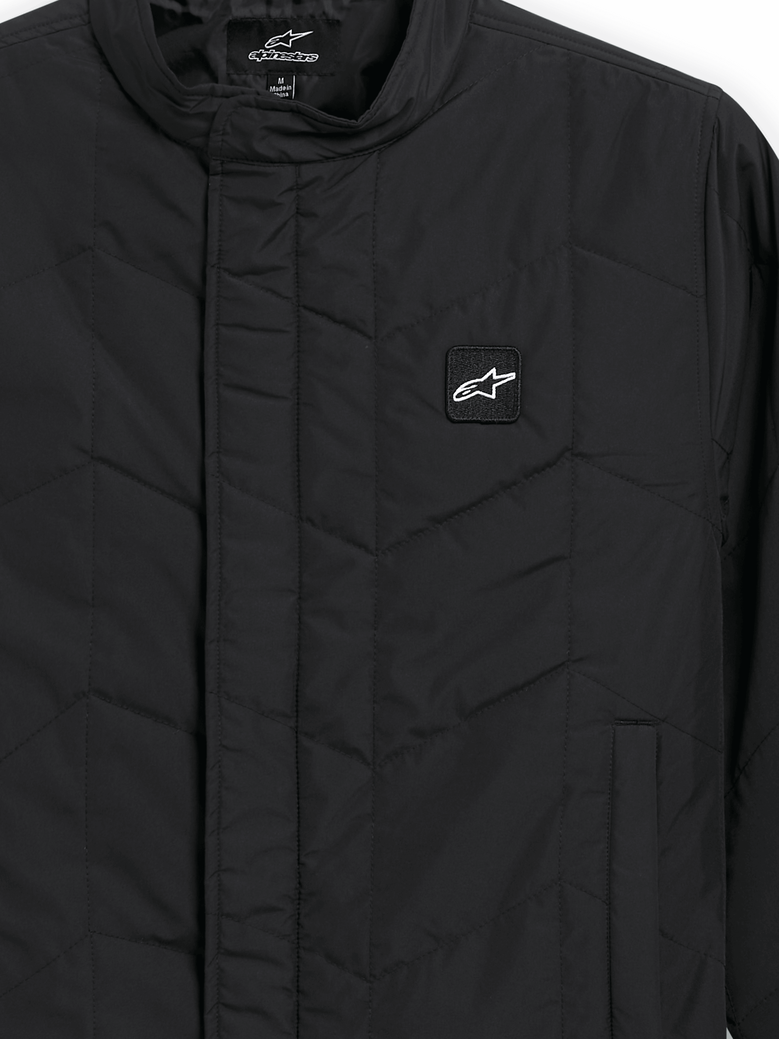 Alpinestars Precedent Jacke, gesteppte Sportswear-Jacke, Schwarz, Nahaufnahme mit ikonischem schrägem Steppmuster, niedrigem Stehkragen, verdecktem Frontreißverschluss und kleinem Logo-Patch auf der Brust