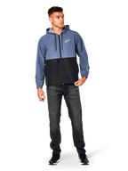 Alpinestars Speeder Windbreaker-Jacke, Schieferblau und Schwarz, leichte Kapuzenjacke mit Mesh-Futter, weißes Stern-Logo auf der Brust, getragen mit schwarzen Jeans und Sneakern, lässiges Motorsport-Streetwear-Design.