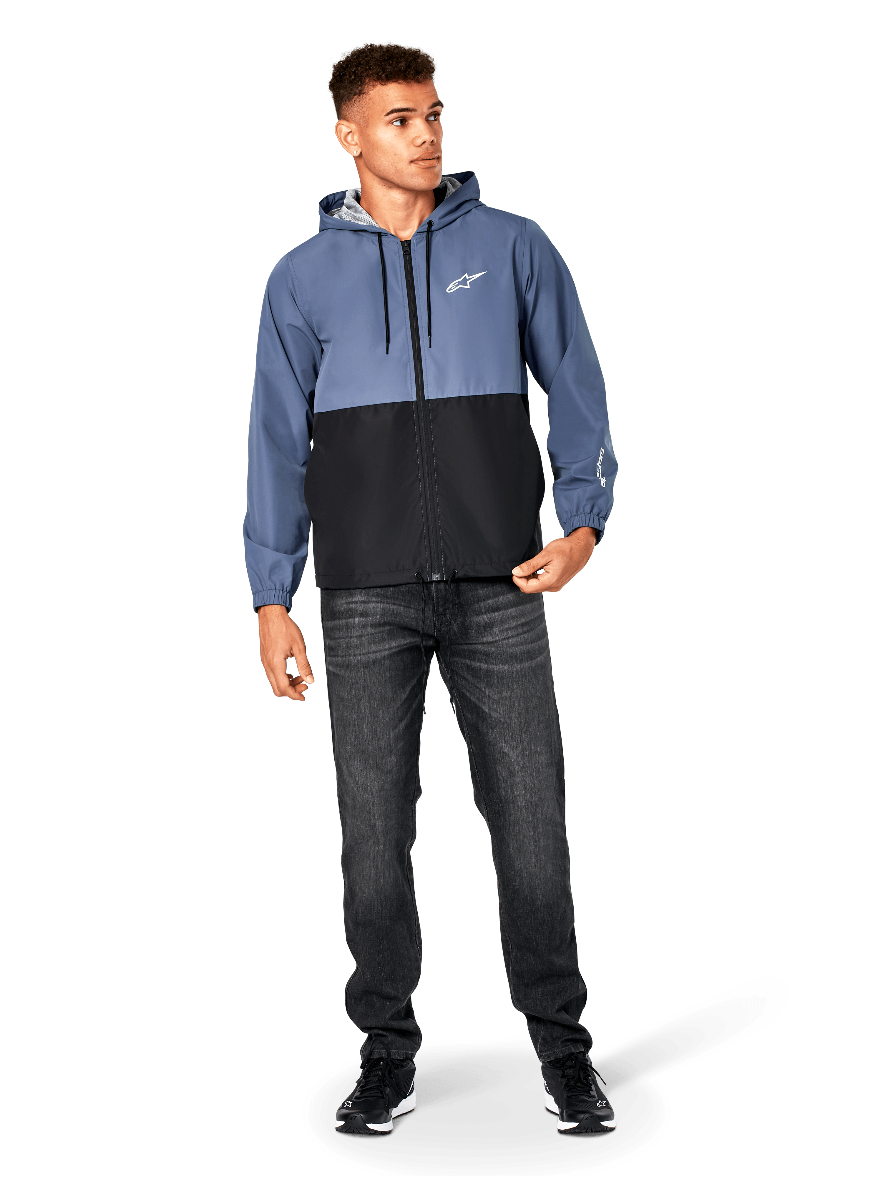 Alpinestars Speeder Windbreaker-Jacke, Schieferblau und Schwarz, leichte Kapuzenjacke mit Mesh-Futter, weißes Stern-Logo auf der Brust, getragen mit schwarzen Jeans und Sneakern, lässiges Motorsport-Streetwear-Design.