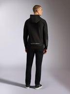 Alpinestars Sessions V3 Hoodie, lässige Streetwear, Schwarz mit grauem Alpinestars-Schriftzug am unteren Rücken und „astars“-Branding auf den Ärmeln, Rückansicht eines männlichen Models in Hoodie und schwarzer Hose, modernes, vom Motorsport inspiriertes Design