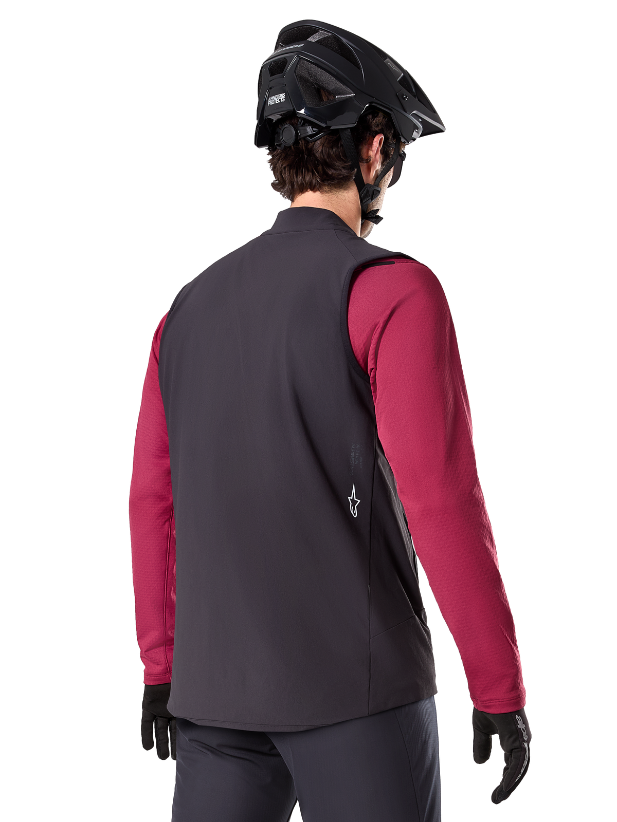 Alpinestars A-Dura Thermoweste, Schwarz, Rückansicht, getragen über einem weinroten Langarmtrikot mit einem schwarzen Mountainbike-Helm und Handschuhen, leichte isolierte Fahrradausrüstung für Offroad-Fahrten