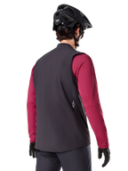Alpinestars A-Dura Thermoweste, Schwarz, Rückansicht, getragen über einem weinroten Langarmtrikot mit einem schwarzen Mountainbike-Helm und Handschuhen, leichte isolierte Fahrradausrüstung für Offroad-Fahrten