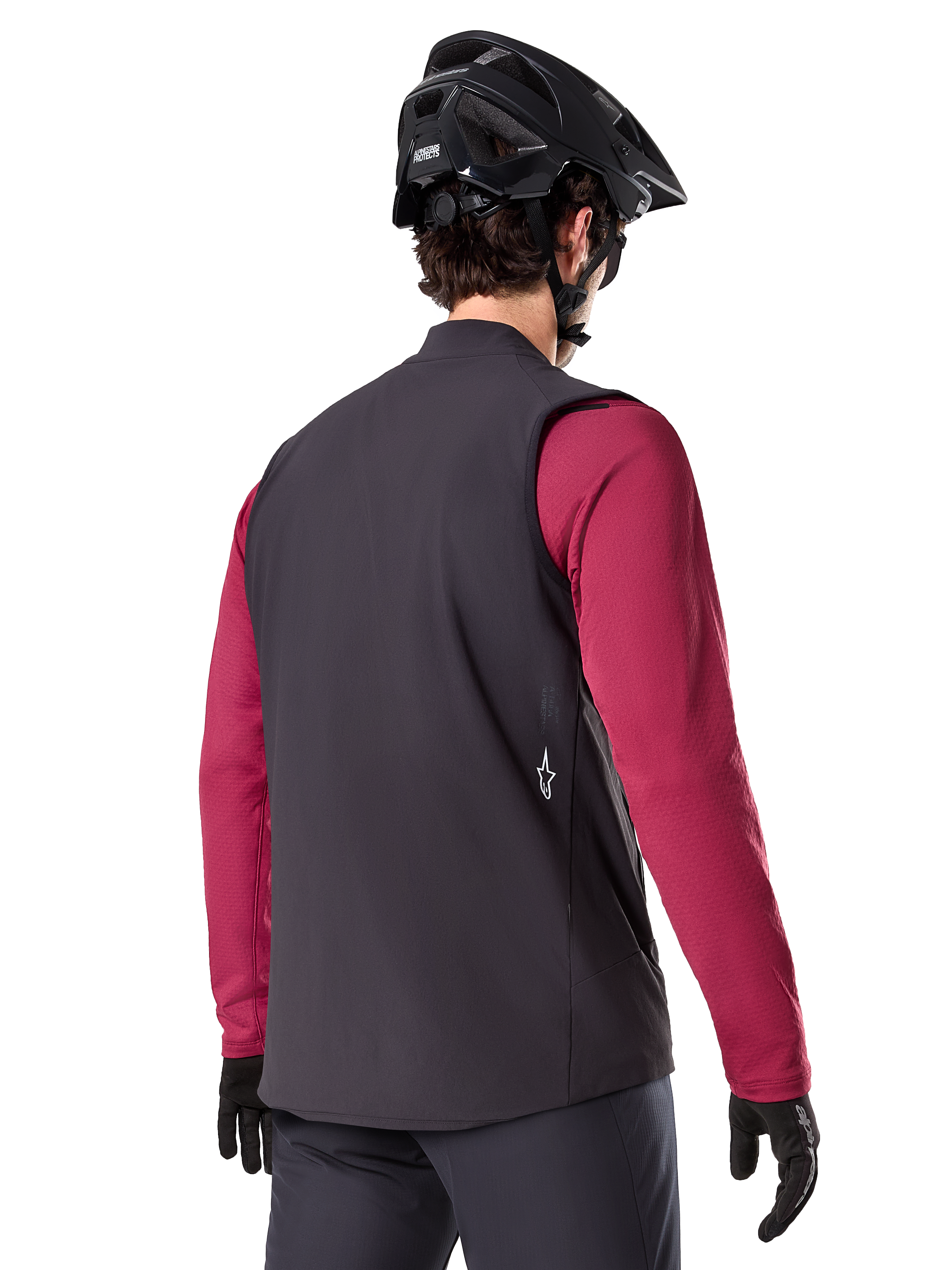 Alpinestars A-Dura Thermoweste, Schwarz, Rückansicht, getragen über einem weinroten Langarmtrikot mit einem schwarzen Mountainbike-Helm und Handschuhen, leichte isolierte Fahrradausrüstung für Offroad-Fahrten