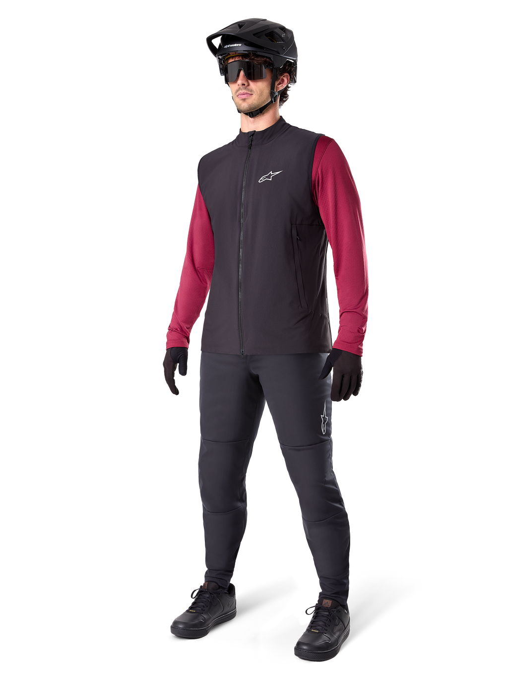 Alpinestars A-Dura Thermoweste, schwarze Fahrradweste, getragen von einem Fahrer über einem weinroten Langarmtrikot und schwarzer Hose, mit schwarzem MTB-Helm und Handschuhen, entworfen für das Mountainbiken bei kaltem Wetter
