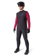Alpinestars A-Dura Thermoweste, schwarze Fahrradweste, getragen von einem Fahrer über einem weinroten Langarmtrikot und schwarzer Hose, mit schwarzem MTB-Helm und Handschuhen, entworfen für das Mountainbiken bei kaltem Wetter