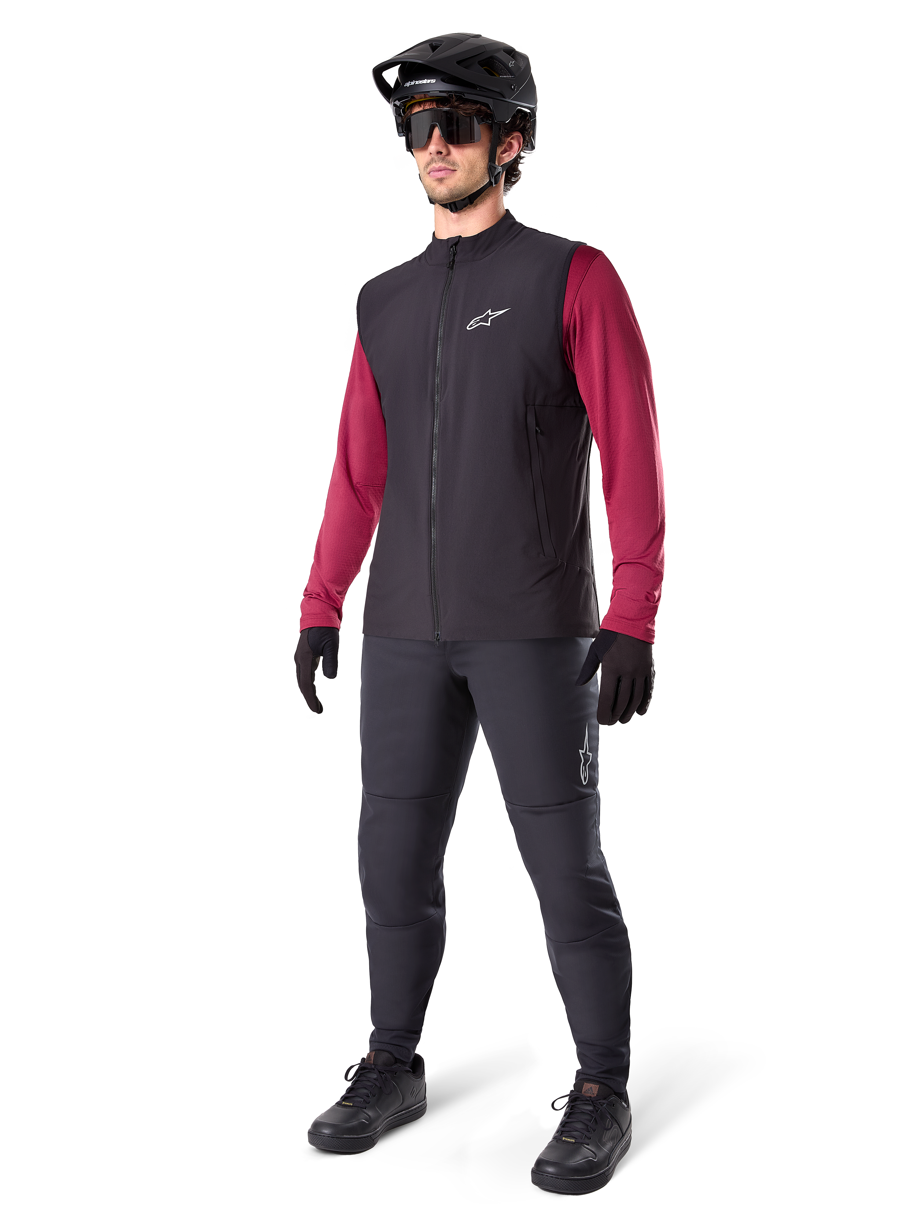 Alpinestars A-Dura Thermoweste, schwarze Fahrradweste, getragen von einem Fahrer über einem weinroten Langarmtrikot und schwarzer Hose, mit schwarzem MTB-Helm und Handschuhen, entworfen für das Mountainbiken bei kaltem Wetter